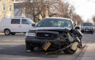 Black Ford sedan with significant front-end damage on a city street, representing the aftermath of a car accident.