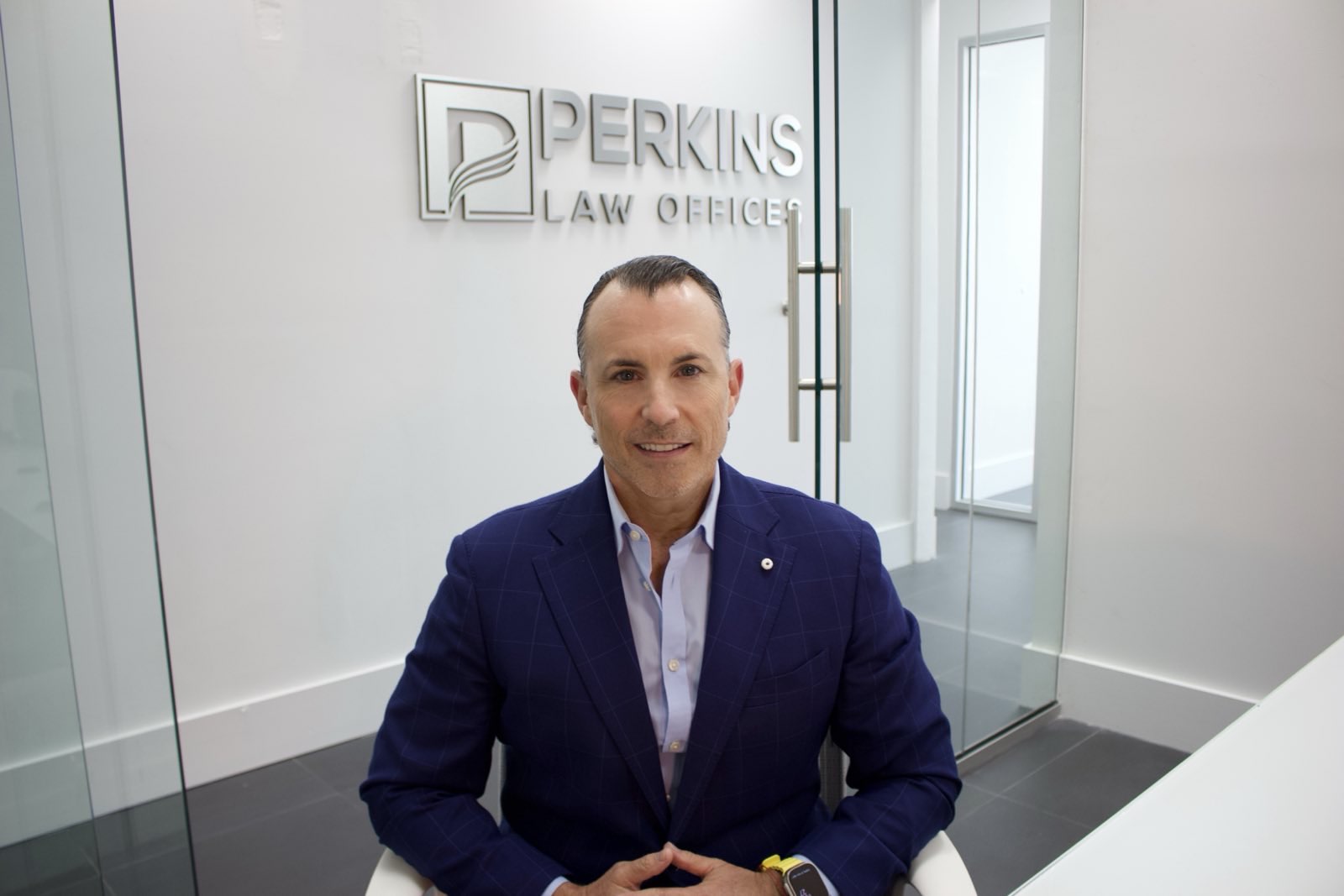 Alex Perkins, President of Perkins Law Offices, seated in a modern office setting, showcasing the firm's logo in the background, emphasizing expertise in personal injury law.