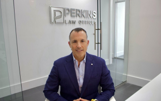 Man sitting at a desk in Perkins Law Offices, Miami, with a modern office backdrop and the firm's logo visible, representing personal injury legal services.
